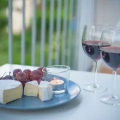 Dwa kieliszki czerwonego wina, talerz z serem camembert, winogronami i świecą.